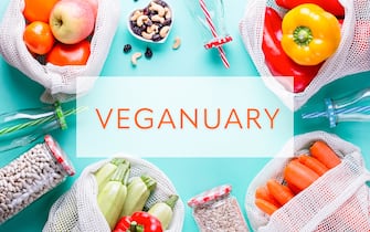 Veganuary background on light blue with fresh fruits and raw vegetables in eco mesh bags, top view, veganuary quote