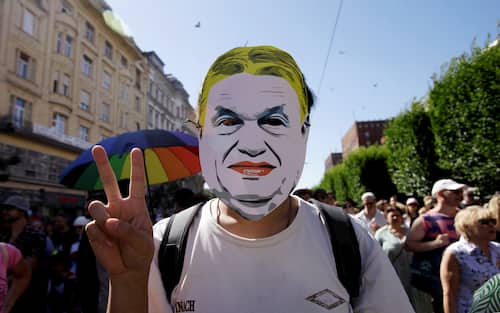 A participant wearing a mask depicting Hungary's Prime Minister Viktor Orban flashes the victory sign during the Budapest Pride march, on June 28, 2025 in Budapest, despite a governmental ban of the event. Hungary's Prime Minister had announced that police will not "break up" Saturday's Budapest Pride march despite issuing a ban, but warned attendees and organisers about the legal consequences. His ruling coalition amended laws and the constitution earlier this year to prohibit the annual celebration, advancing his widely condemned, years-long clampdown on LGBTQ rights in the name of "child protection". (Photo by Peter Kohalmi / AFP)