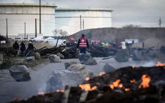 TOPSHOT - A unionist of the French union General Confederation of Labour (CGT) stands close to burning debris and a makeshift barrier blocking the access to the oil terminals at the Total Energies refinery during a protest against the government's proposed pensions overhaul in Donges, western France on March 17, 2023. (Photo by LOIC VENANCE / AFP)