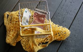 The Global Food Crisis. Saving Money, Inflation And Responsible Consumerism. Yellow Reusable Bag And Empty Metal Market Cart Cause Only 15 Euros For Shopping. Ambient Light, Copy Space