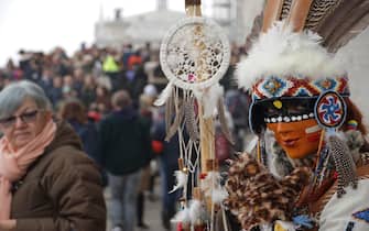 Un personaggio, vestito di un costume ispirato ai nativi nordamericani,  posa tra la folla di turisti accalcati sul ponte della Paglia, per il carnevale veneziano, oggi 18 febbraio 2023. ANSA/ANDREA MEROLA