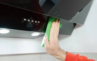 Aspirator cleaning, young man cleans a glossy black extractor hood in a modern kitchen, dusting and wiping
