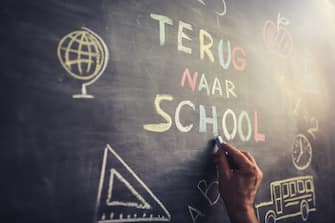 Hand writing â  Terug naar Schoolâ   multicoloured words blackboard (Back to School in dutch language . She is also drawing a school bus, an apple, a mathematical formula and other school related symbols.