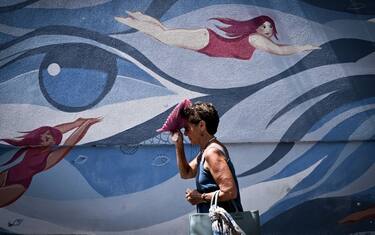 TOPSHOT - A pedestrian shelters from the sun with a handheld fan as she walks past a mural by the artists Maria Ginzburg and Gaetano Matrella, downtown Rome, on July 19, 2023, amid a heat wave in Italy. (Photo by Tiziana FABI / AFP) / RESTRICTED TO EDITORIAL USE - MANDATORY MENTION OF THE ARTIST UPON PUBLICATION - TO ILLUSTRATE THE EVENT AS SPECIFIED IN THE CAPTION (Photo by TIZIANA FABI/AFP via Getty Images)