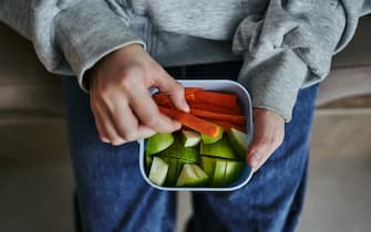 Close-up of a lunch box in the hands of a child with healthy food, nuts, carrots and an apple. Top view