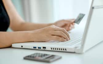 Woman makes online purchases sitting in front of laptop with bank card in her hand. Hands close-up. Concept of online shopping and money transfer.