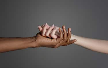 White caucasian hand in black afro american hand holding together on grey background.