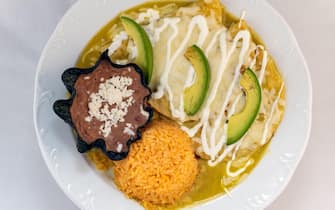 Overhead view of enchiladas Suizas served with rice and tortilla chip bowl refried beans looks and tastes appealing.