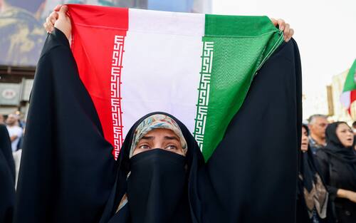An Iranian woman lifts a national flag during a rally protesting the US attack on Iran in Enghelab Square in Tehran on June 22, 2025. Iran's President Masoud Pezeshkian condemned US strikes on nuclear sites on June 22, saying in his first response that the attack revealed Washington was "behind" Israel's military campaign in the Islamic republic. (Photo by ATTA KENARE / AFP)