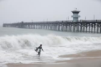 epa10811128 A surfer runs out of the water in Seal Beach, California, USA, 20 August 2023. Southern California is under a tropical storm warning for the first time in history as Hilary makes landfall. The last time a tropical storm made landfall in Southern California was 15 September 1939, according to the National Weather Service.  EPA/CAROLINE BREHMAN