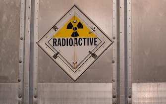 A Bright yellow and black radioactive warning symbol known as a Trefoil on the back of a stainless steel truck trailer.