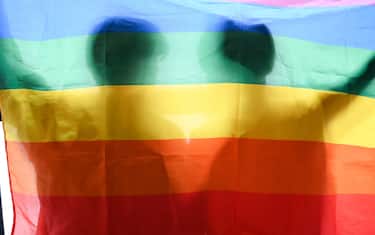 Two gay men friends holding a LGBT flag. LGBT rainbow flag with human shadow.  LGBT pride parade.