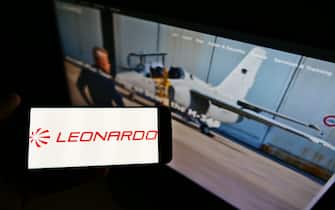 Person holding mobile phone with logo of Italian defense company Leonardo S.p.A. on screen in front of business webpage. Focus on cellphone display.