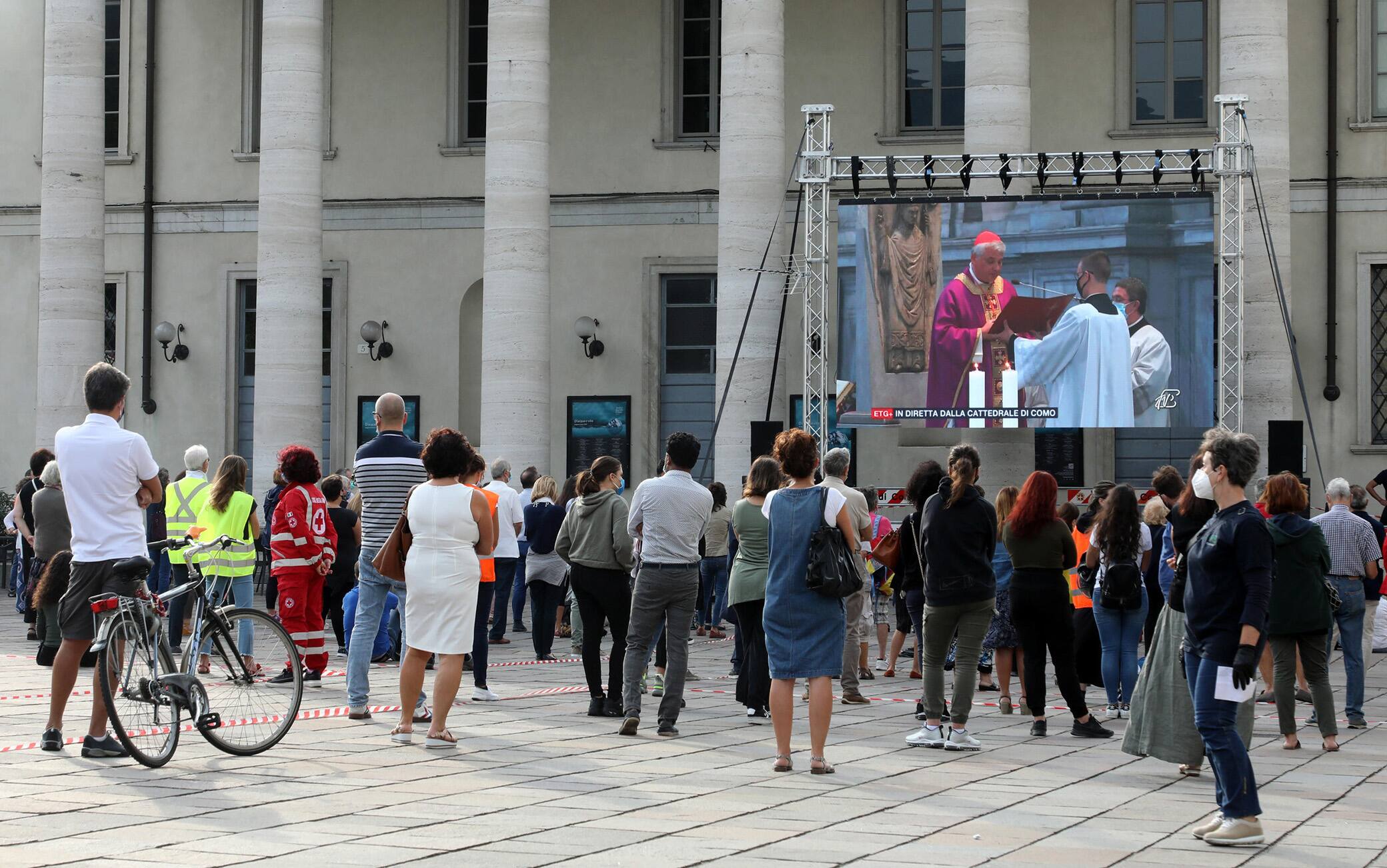 Alcune persone seguono su uno dei maxi schermi che sono stati allestiti nel centro di Como in occasione dell'orazione funebre per don Roberto Malgesini il parrocco assassinato da una delle persone di cui si prendeva cura. Como 19 Settembre 2020.
ANSA / MATTEO BAZZI