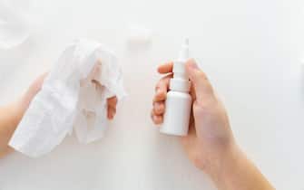Child hands hold bottle nose spray and paper tissue on white background. Runny nose treatment