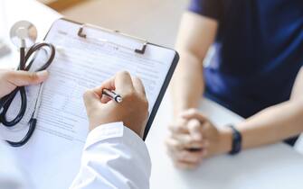 Close-up of a male doctor hand hold a silver pen and showing pad in hospital. Doctor giving prescription to the patient and filling up medical form at a clipboard