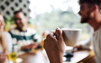 Close up of happy woman drinking coffee while talking to her friends in a cafe.