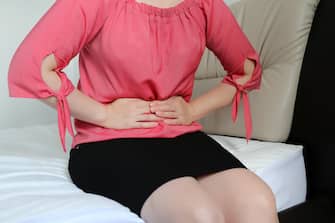 Woman suffering from abdominal pain. Slim girl sitting on bed at home clutching her abdomen, concept of stomach ache, illness, menstruation