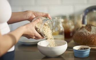 Close up of a woman preparing a wholesome breakfast by pouring oats into a bowl from a plastic free jar with fresh berries.