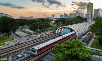 A high view point of Singapore mass rapid transit  (MRT) transportation train service in central Kallang station during sunset with Singapore city skyline in background. Singapore MRT train system serves as one of Singapore daily transportation for most commuters. Background include Singapore downtown city skyline with modern skyscrapers and commercial buildings such as Marina Bay Sands and Singapore flyer