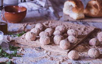 Raw meatballs on a wooden cutter and other ingredients on a kitchen table