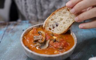dipping a slice of baguette into stewed beef with tomato sauce
