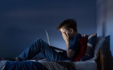 Online bullying Cyber bullying photo of an upset boy in his bedroom looking at hurtful messages on social media