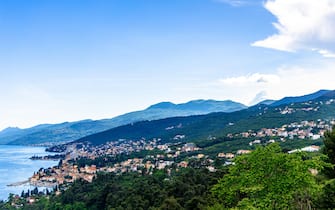 Opatija, Croatia offers a stunning view of the coastline, mountains, city buildings, vegetation, and the Adriatic Sea on a bright, sunny day.