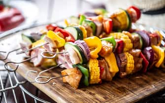 Pile of skewers with chicken meat, bacon, and vegetables such as corn, peppers, onions is ready to be put on a barbeque. 
