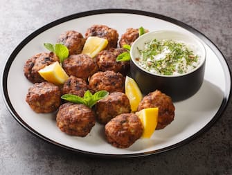 Keftedakia is a Greek traditional dish that is created with minced beef and bread crumbs rolled into balls and fried closeup on a white plate on a table. Horizontal
