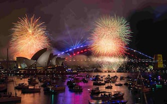 The "family fireworks", displayed three hours before midnight every year ahead of the main show at midnight, fill the sky over the Opera House (L) and Sydney Harbour Bridge (R) in Sydney on New Year's Eve on December 31, 2023. (Photo by Izhar KHAN / AFP)