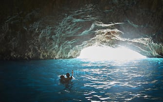 Young multiracial couple swimming in sea inside cave filming on camera during vacation