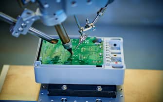 Robotic arm welding and installing component at semiconductor circuit board on workbench.