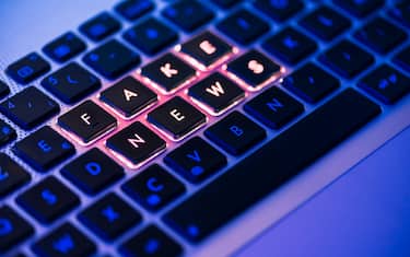 Fake news written in red on a backlit laptop keyboard close-up with selective focus in a blue ambiant light