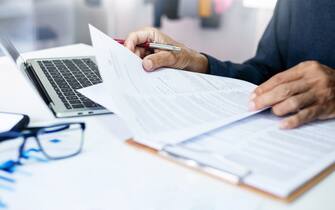 Asian businessman reviewing document reports at office workplace with computer laptop. legal expert, professional lawyer reading and checking financial documents or insurance contract