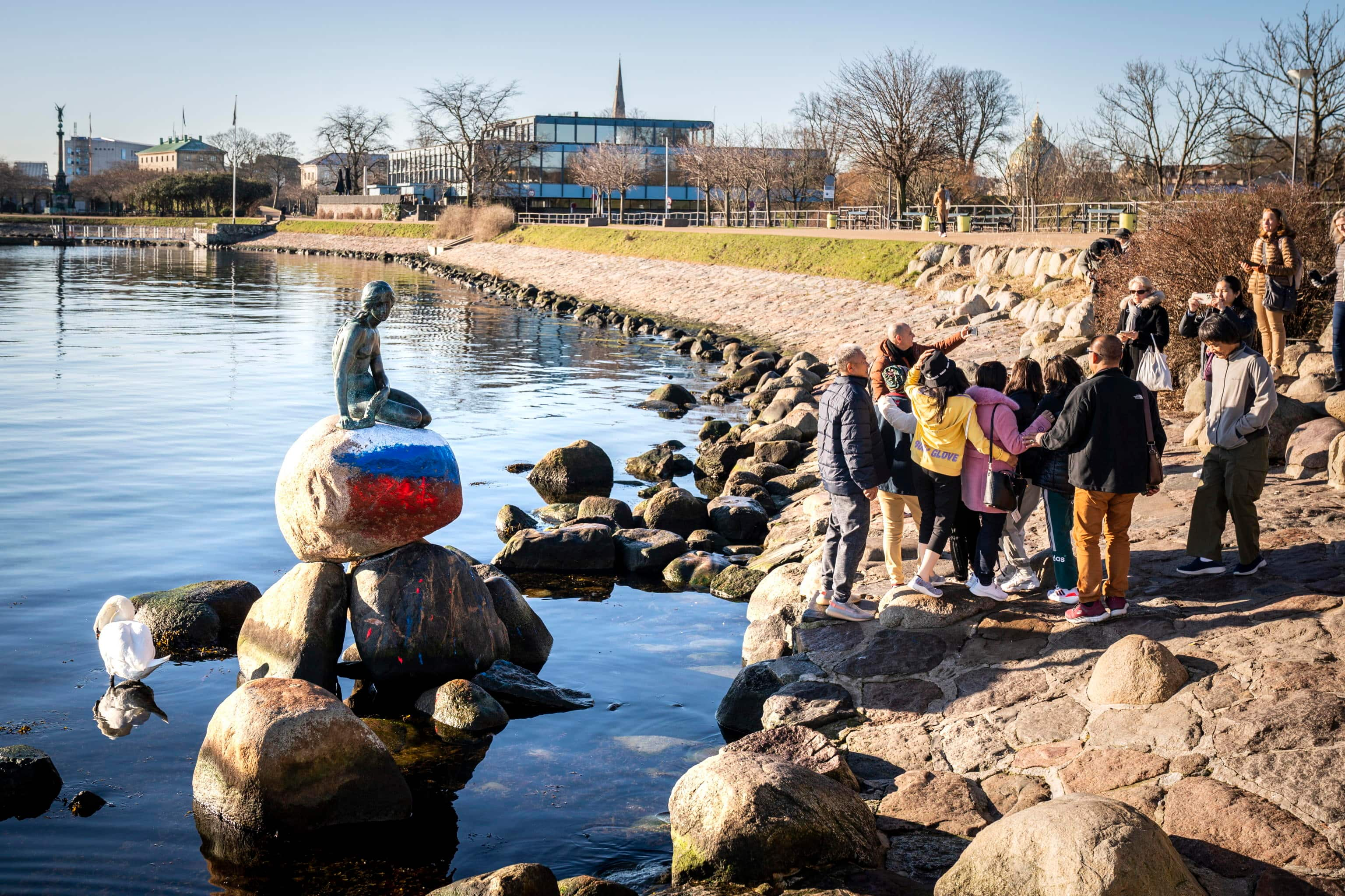 epa10498414 People pose for a picture with the vandalized Little Mermaid statue, with the Russian flag painted on the stone where it sits on, in Copenhagen, Denmark, 02 March 2023. The Little Mermaid was created by the sculptor Edvard Eriksen and modeled after his wife, Eline. The figure is the sculptor's embodiment of the mermaid in Hans Christian Andersen's famous fairy tale 'The Little Mermaid'.  EPA/IDA MARIE ODGAARD  DENMARK OUT