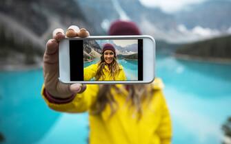 A young woman in a yellow jacket taking a cell phone selfie
