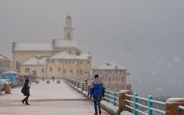 GENOA, ITALY - JANUARY 23: Tourists walk under snowfall at Boccadasse beach on January 23, 2019 in Genoa, Italy. A cold snap has hit Italy this week with snow forecast in Florence, Bologna, Genoa and other cities. (Photo by Awakening/Getty Images)