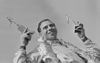 British Formula One racing driver Jim Clark (1936-1968) celebrates on the podium with two statuettes after finishing in first place in the #4 Team Lotus Lotus 25 Climax V8 to win the 1963 British Grand Prix at Silverstone Circuit in Northamptonshire, England on 20th July 1963. (Photo by Blackman/Express/Hulton Archive/Getty Images)