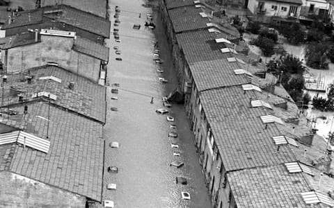 A boat moves along a street turned into a canal by the flood, from which the roofs of the parked car emerge. Florence, 1966. (Photo by Giorgio Lotti Mario De Biasi Sergio Del Grande/Mondadori via Getty Images)