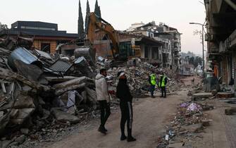 epa10467151 People walk at the site of collapsed buildings after a powerful earthquake, in Hatay, Turkey, 14 February 2023. More than 37,000 people died and thousands more were injured after two major earthquakes struck southern Turkey and northern Syria on 06 February. Authorities fear the death toll will keep climbing as rescuers look for survivors across the region.  EPA/SEDAT SUNA