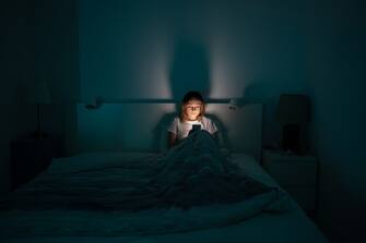 Sleepy exhausted woman lying in bed using smartphone, can not sleep. Insomnia, addiction concept. Sad girl bored in bed scrolling through social networks on mobile phone late at night in dark bedroom.