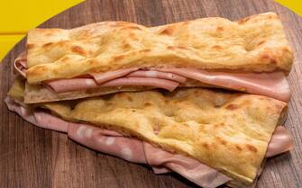 two focaccia bread sandwich filled with bologna mortadella on wooden cutting board and yellow background