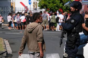 A police officer interacts with a man as others queue to enter a supermarket in the Magenta district of Noumea, France's Pacific territory of New Caledonia, on May 18, 2024. Anger over France's plan to impose new voting rules has spiralled into the deadliest violence in four decades in the archipelago of 270,000 people, which lies between Australia and Fiji -- 17,000 kilometres (10,600 miles) from Paris. (Photo by Theo Rouby / AFP) (Photo by THEO ROUBY/AFP via Getty Images)