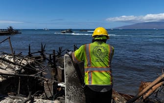 epa10796020 A public works worker looks at a burnt sunken boat in the port of Lahaina, Hawaii, USA, 11 August 2023. At least 67 people were killed in the wildfires burning in Maui, which is considered the largest natural disaster in Hawaii's state history.  EPA/ETIENNE LAURENT