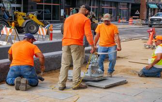 Construction workers using electric suction lifter to place pavement blocks on Lake Street Reconstruction Project. Oak Park, Illinois.