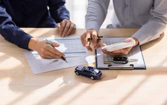 Dealer salesman giving car key to owner. client signing insurance document or rental car lease form agreement contract Insurance car concept.