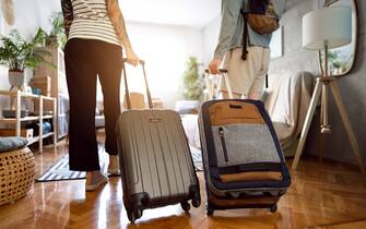 Rear-view of an unrecognizable couple arriving at the accommodation with their suitcases