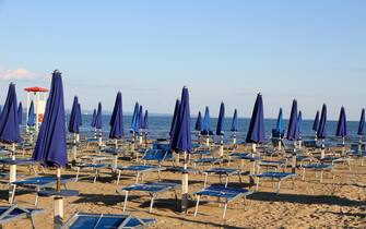 Many umbrellas and deckchairs on the beach at sunset on the seashore with the lookout tower