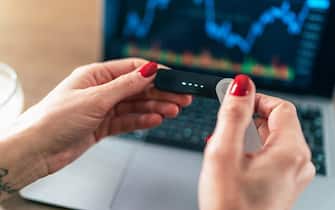Female hand holding Digital wallet for cryptocurrency in front of laptop. Unrecognisable woman working on a laptop and holding digital crypto wallet. Hands of a woman using hardware wallet buy cryptocurrency, blockchain investment.